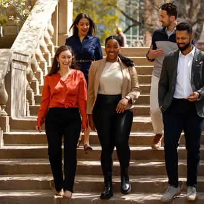 Five students-two men and three women--walk down steps on campus laughing and talking on a sunny day