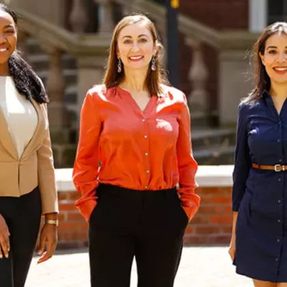 Three women stand in the quad, smiling at the camera